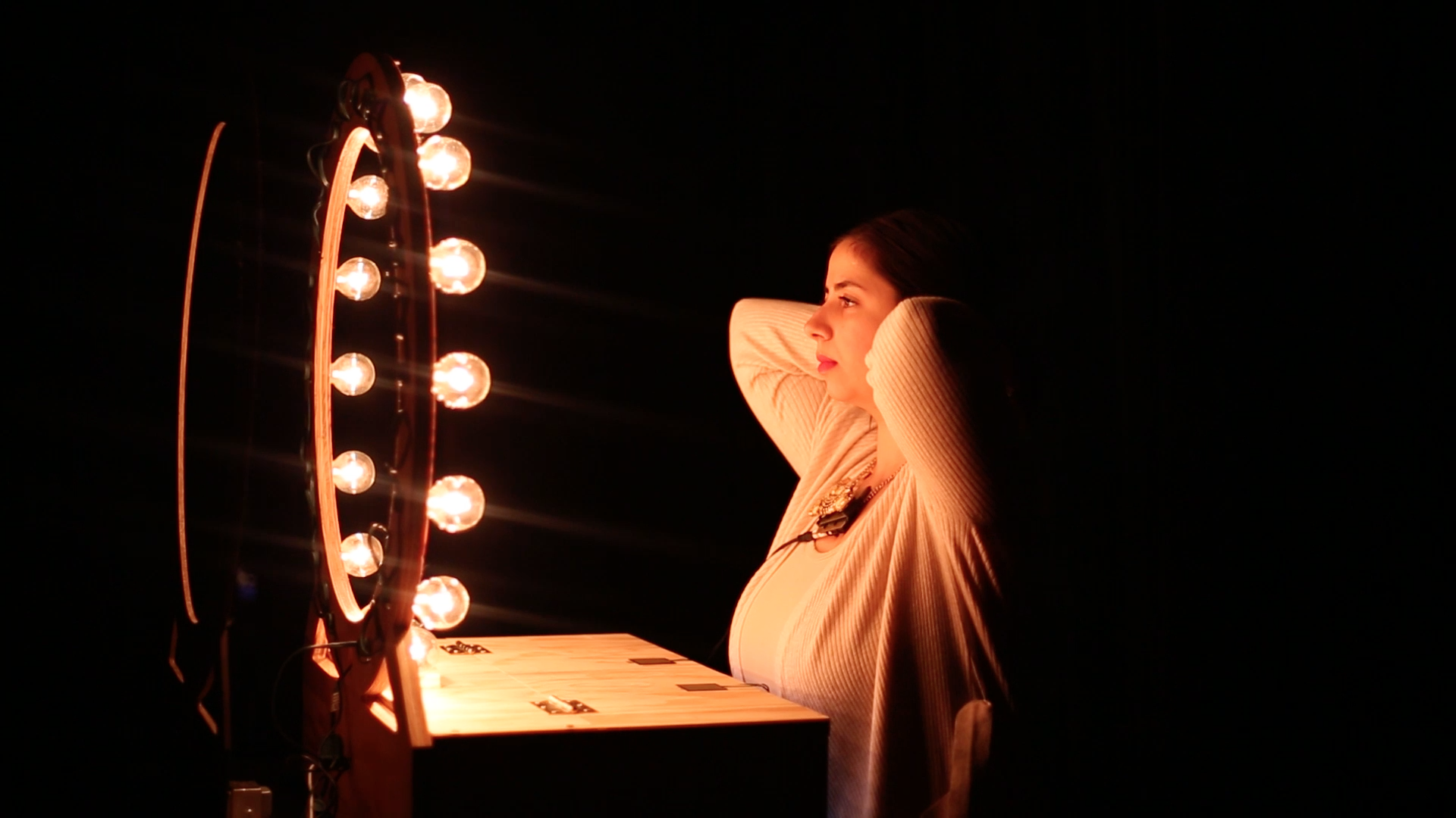 Photo of the performance. The artist is behind a ring light and she is putting an analog synthesizer necklace on.